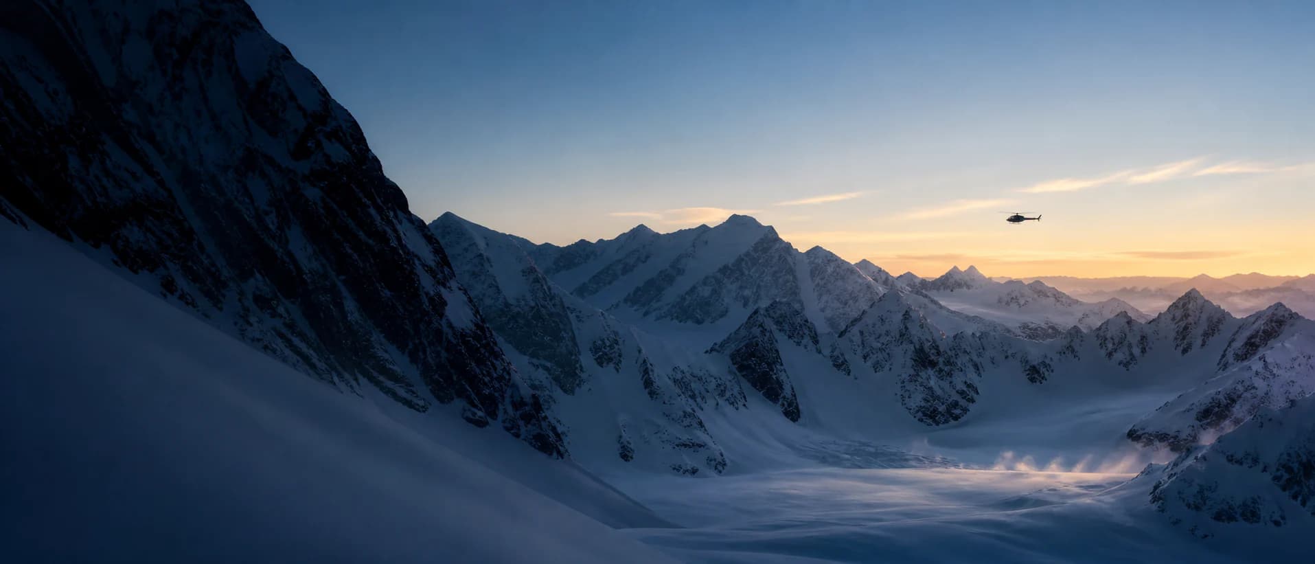 A helicopter flying across a glaciated mountain range